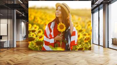 Beautiful girl in hat with the American flag in a sunflower field. 4th of July. Fourth of July. Freedom. Sunset light The girl smiles. Beautiful sunset. Independence Day. Patriotic holiday.  Wall mural