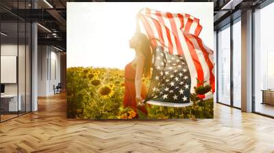 Beautiful girl with the American flag in a sunflower field. 4th of July. Fourth of July. Freedom. Sunset light The girl smiles. Beautiful sunset. Independence Day. Patriotic holiday. Wall mural