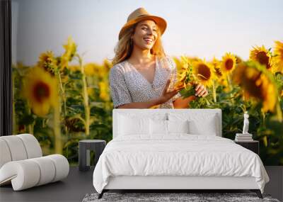 Beautiful woman posing in a field of sunflowers in a dress and hat.  Fashion, lifestyle, travel and vacations concept. Wall mural