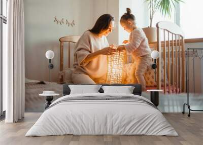 Cheerful mother and her little daughter watching at the lamp. Happy young woman and her little cute daughter enjoy the night light. Happy loving family.  Wall mural