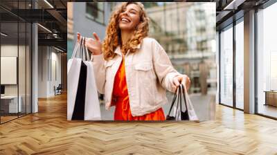 Cheerful woman holding shopping bags. Beautiful woman in casual style shopping in the city. Consumerism, purchases, shopping, lifestyle, sale concept Wall mural