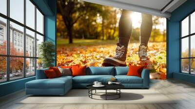 Close-up of female legs in hiking boots walks on ground with yellow-orange dry fall leaves during autumn season in park or forest. Feet walking in outdoor nature. Healthy lifestyle on leisure activity Wall mural