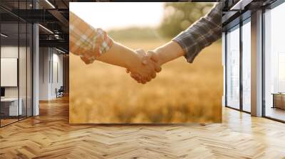 Close-up of two farmers shaking hands in a golden wheat field. Farmers in an agricultural field make an agreement with a handshake. Business concept, agriculture. Wall mural