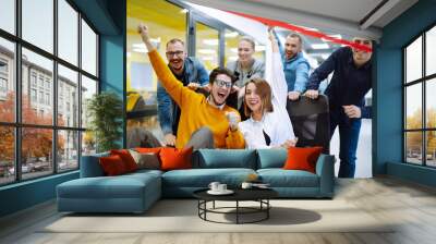 Friendly work team  ride chairs in office room cheerfully excited diverse employees laugh while enjoying fun work break activities, creative friendly workers play a game together. Wall mural