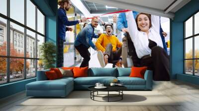 Friendly work team  ride chairs in office room cheerfully excited diverse employees laugh while enjoying fun work break activities, creative friendly workers play a game together. Wall mural