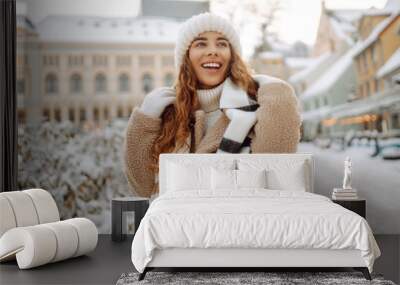 Happy woman having fun on a snowy street on a frosty morning in winter. A young woman walks through the city on a winter day. Concept of walks, weekends. Wall mural