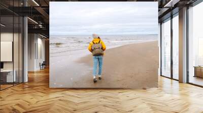 Happy woman in a yellow coat walks along the seashore.  Travel, tourism concept. Active lifestyle. Wall mural