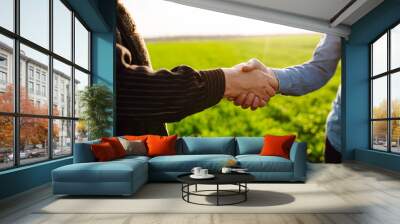 Negotiation. Two farmers agree by shaking hands in a green wheat field. The concept of agricultural business. Wall mural