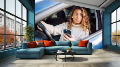 Portrait of a young woman texting on her smartphone while driving a car. Car sharing, rental service or taxi app. Wall mural