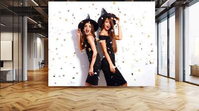 portrait two happy young women in black witch halloween costumes on party over white background. firecrackers in the background. confetti . the concept of Halloween . funny faces  Wall mural