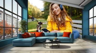 Pretty young womanusing mobile phone in the city while listening music through earphones to go by the bicycle in the park. Lifestyle. Relax, nature concept. Wall mural