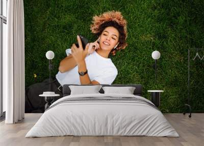 Smiling woman using a smart phone and relaxing at the park on green grass. Concept of leisure, youth, lifestyle. Wall mural