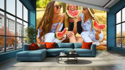 Three beautiful young girls have fun together and eating watermelon  in hot summer day. Friends holding slice of watermelon and posing in the park. Summer concept.  Wall mural