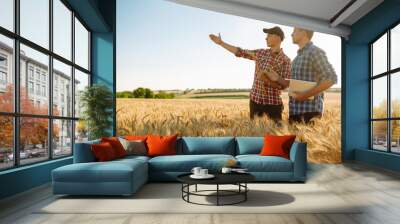 Two young farmers standing in wheat field examining crop holding tablet using internet. Modern agriculture technology. Smart farming concept.  Wall mural