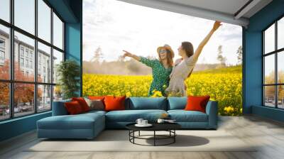 Two young women in a beautiful field with yellow flowers. They jump and have fun. Friendship Day Wall mural