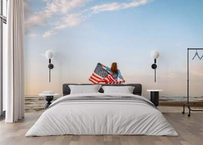 Young woman holding national American flag cover ocean beach holiday travel at summer romantic sunset. America independence day concept. 4th of July. Wall mural