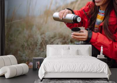 Young woman holds a thermos and drinks tea in autumn forest. Rest, relaxation, travel, lifestyle concept. Wall mural