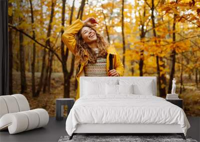 Young woman in a yellow raincoat exploring a vibrant autumn forest filled with colorful foliage during a sunny afternoon hike. Autumn landscape. Wall mural