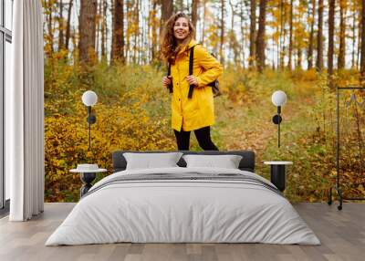 Young woman in a yellow raincoat exploring a vibrant autumn forest filled with colorful foliage during a sunny afternoon hike. Autumn landscape. Wall mural