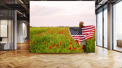 Young woman proudly hold waving american USA flag in in the poppy field. Patriot raise national american flag against the blue sky. Independence Day, 4th July. Wall mural