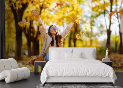 Young  woman smiling and throwing maple leaves up in the air. Wall mural