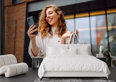 Young Woman use of mobile phone and hold with shopping bag. Consumerism, sale, black friday. Online shopping. Wall mural