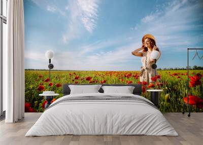 Young woman walking in amazing poppy field. Summertime. Beautiful woman posing in the blooming poppy field. Nature, vacation, relax and lifestyle. Wall mural