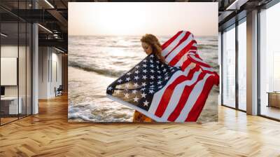 Young woman with american flag on the beach at sunset. 4th of July. Independence Day. Patriotic holiday. Wall mural