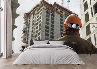 An engineer in a hard hat inspects the facade of a high-rise building under construction. Wall mural