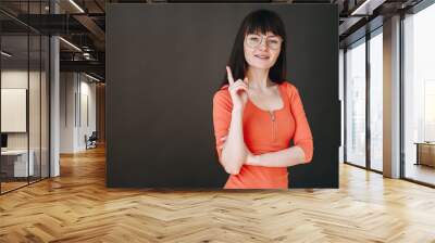 A kind girl with glasses in knitted dress folded her hands and looks at the camera. Modern teacher. Wall mural