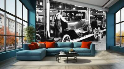 A historical black-and-white photograph of an assembly line with workers building early model cars. The image captures the engineering ingenuity and industrial atmosphere Wall mural