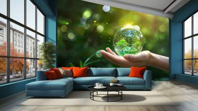 The hands are protecting a globe containing a green tree on an outdoor tropical nature background, Ecology and Environment concept Wall mural