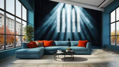 A lone individual stands in a grand cathedral with rays of light streaming through tall, intricate gothic windows, creating a serene and contemplative atmosphere. Wall mural