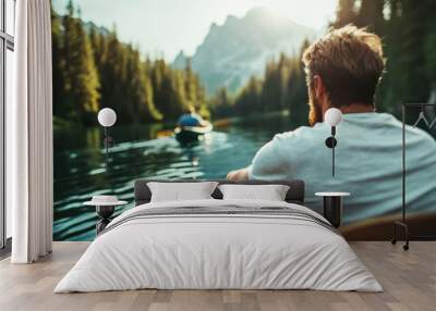 A man enjoys a peaceful kayaking adventure on a calm lake, set against a backdrop of lush evergreen forests and majestic mountains in the morning light. Wall mural