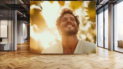 A man savors the sunlight, smiling broadly in a garden filled with lush foliage, representing joy, serenity, and a harmonious connection with nature's beauty. Wall mural