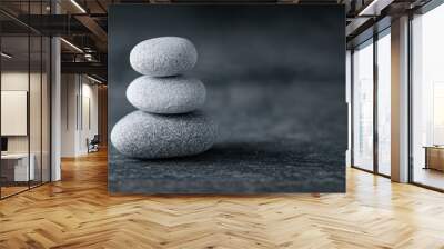 A stack of three smooth grey stones balanced on top of each other against a dark background, symbolizing tranquility, harmony, and balance in life. Wall mural