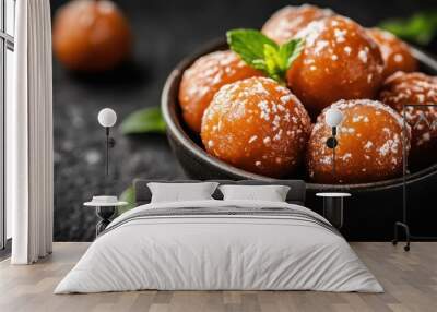 A striking image of perfectly round, golden brown dessert balls coated in powdered sugar, garnished with fresh mint leaves and placed in an elegant black bowl. Wall mural