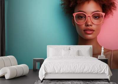 A stylish woman with short, textured hair and glasses poses against a split teal and pink background. Her confident expression and vibrant attire highlight her contemporary style. Wall mural