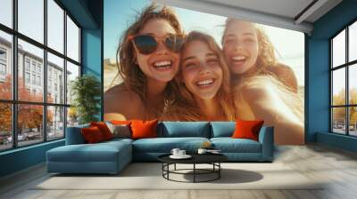 Three friends, with sun-kissed smiles and stylish sunglasses, take a selfie on the beach, perfectly capturing the essence of friendship and summer joy under the sun. Wall mural