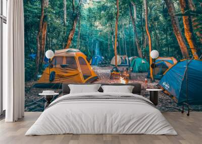 A group of tents are set up in a forest, with a fire burning in the center. The scene is peaceful and serene, with the tents providing a cozy and intimate atmosphere. The fire adds warmth Wall mural