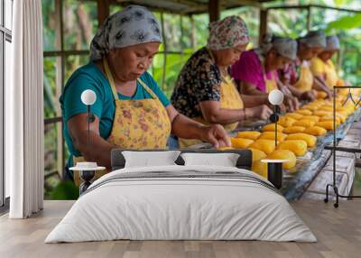 A group of women are working together to make a large batch of yellow pastries. The atmosphere is lively and collaborative, as they work together to create a delicious treat Wall mural