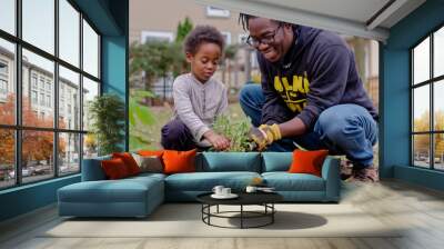 A man and a child are planting a seedling in the dirt. The man is wearing a black hoodie and the child is wearing a white shirt. Scene is happy and playful, as the man Wall mural