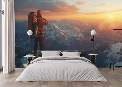 A man with a backpack is standing on a mountain top, looking out at the beautiful sunset. Concept of adventure and awe, as the man takes in the breathtaking view of the mountains and the sky Wall mural