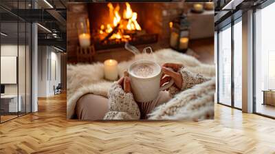 A person is holding a mug of hot chocolate in front of a fireplace. The scene is cozy and warm, with the fire providing a comforting ambiance Wall mural