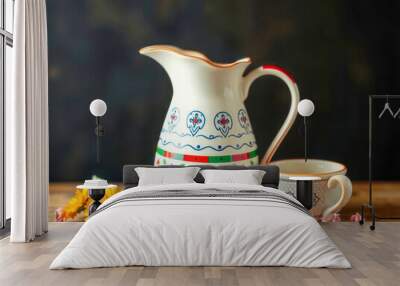 A pitcher with a floral design sits on a wooden table next to a cup. The pitcher is white and has a blue and red design. The table is made of wood Wall mural