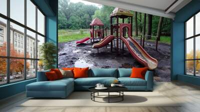 A playground with a slide and a swing set. The slide is wet and the ground is muddy Wall mural