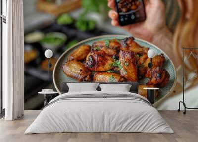 A woman is taking a picture of a plate of chicken wings. The plate is full of wings, and the woman is holding it up for the camera. Concept of indulgence and enjoyment Wall mural