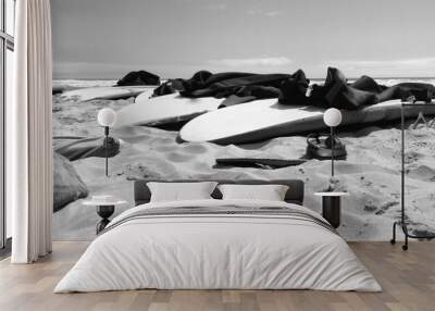 Surfboards and wetsuits lie on the sand Wall mural