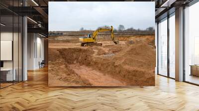 Excavator during earthworks at construction site. Backhoe digging the ground for the foundation and for laying sewer pipes district heating. Earth-moving heavy equipment Wall mural