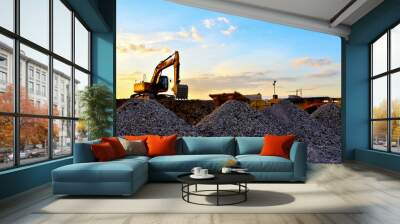 Heavy excavator bucket working in quarry on a background of sunset and blue sky. Mobile jaw stone crusher by the construction site. Crushing old concrete wastes and subsequent cement production Wall mural